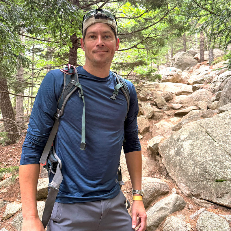 Man wearing deep blue sun shirt hiking in the woods