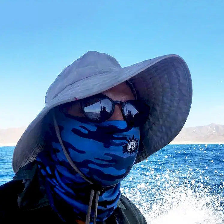man wearing blue camo neck gaiter for sun protection while on a boat ride in the ocean