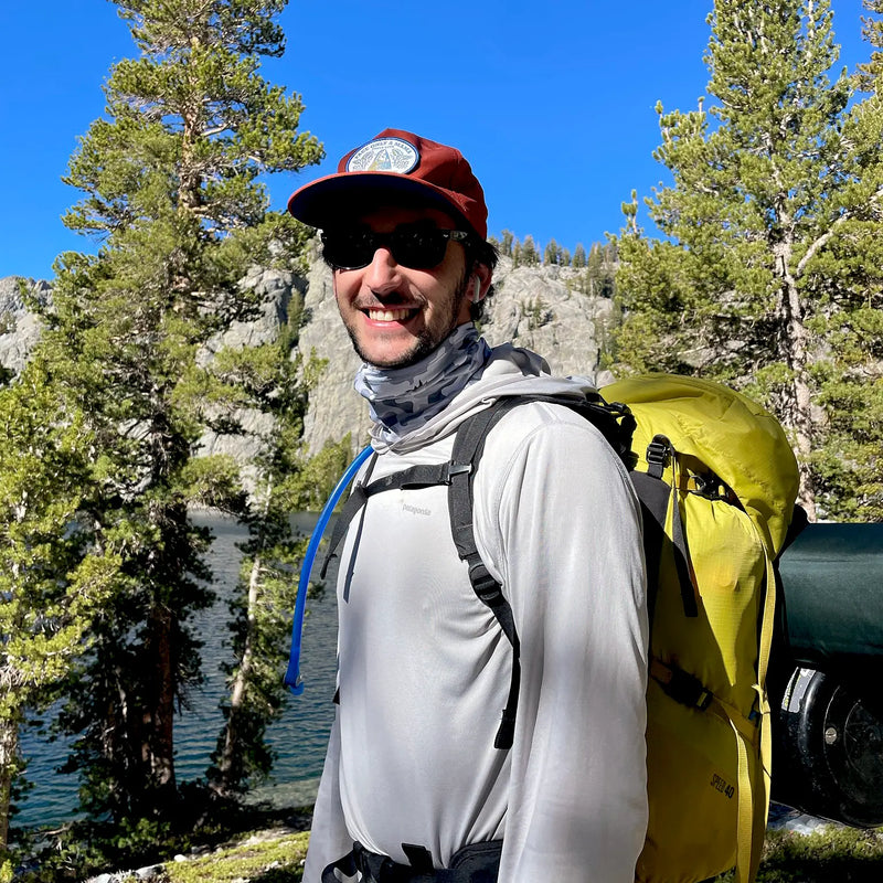 smiling wearing a neck gaiter while hiking in the woods